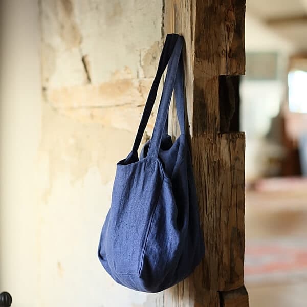 Blue linen tote bag hanging on a rustic wooden post