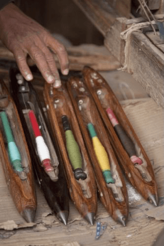 Artisan selecting wooden weaving shuttles with coloured thread