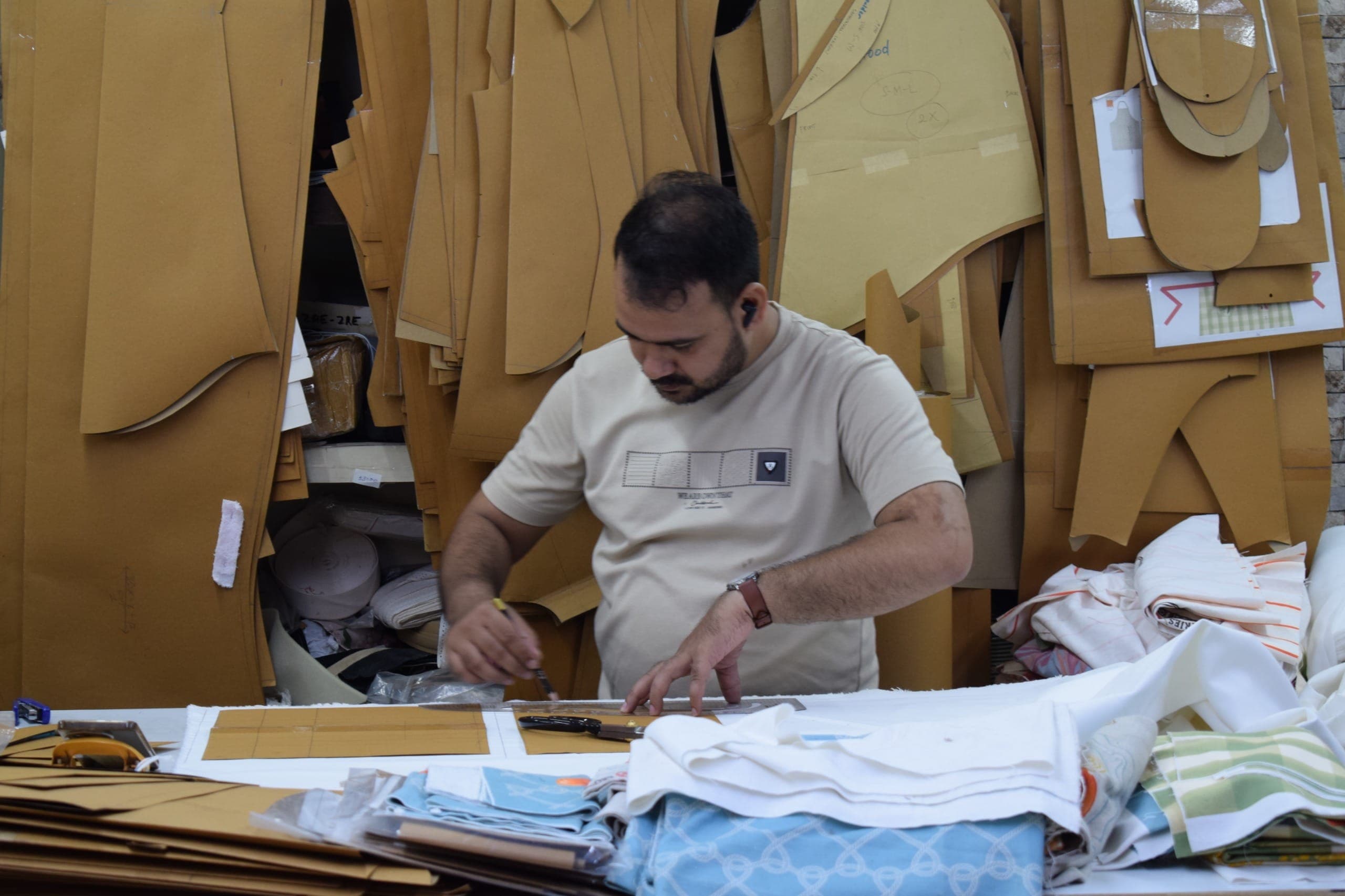 Pattern maker working on a garment pattern at a studio table with fabric samples