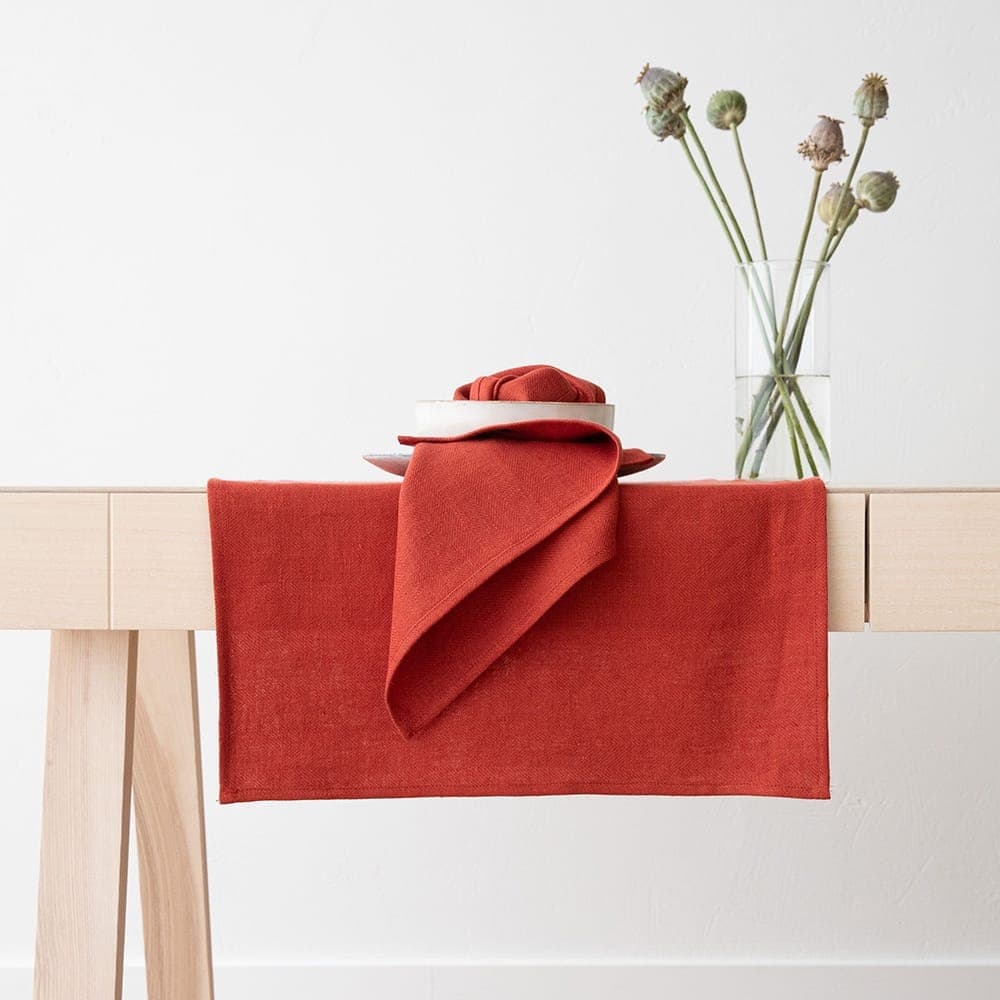 Terracotta linen table runner and napkin on a light wood table