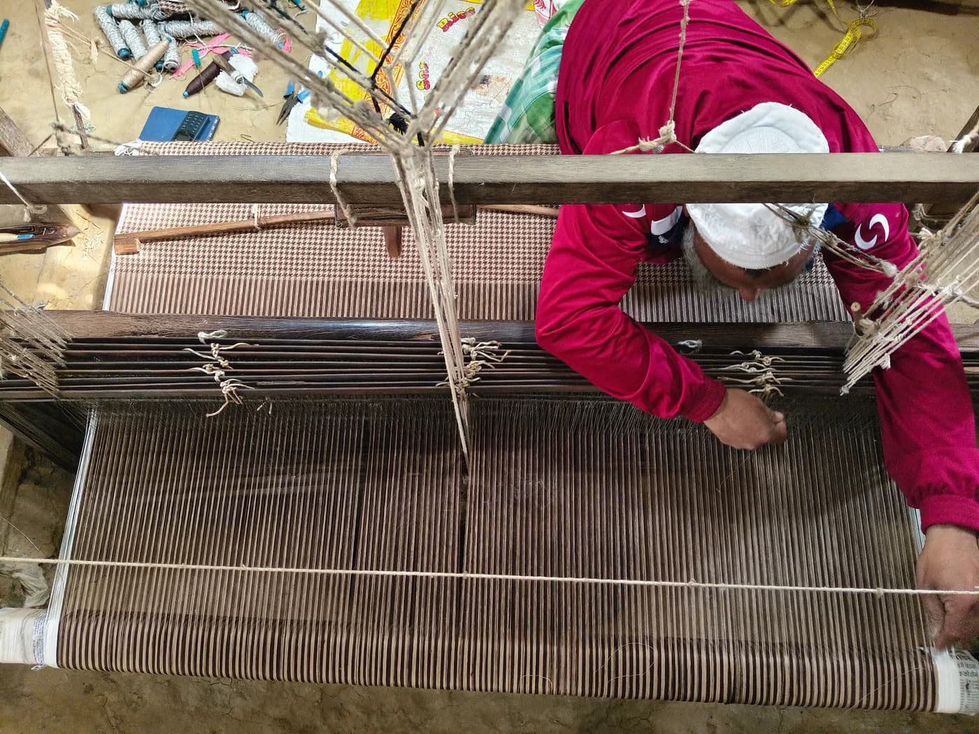 Overhead view of Mubarak weaving fine checkered fabric on a handloom