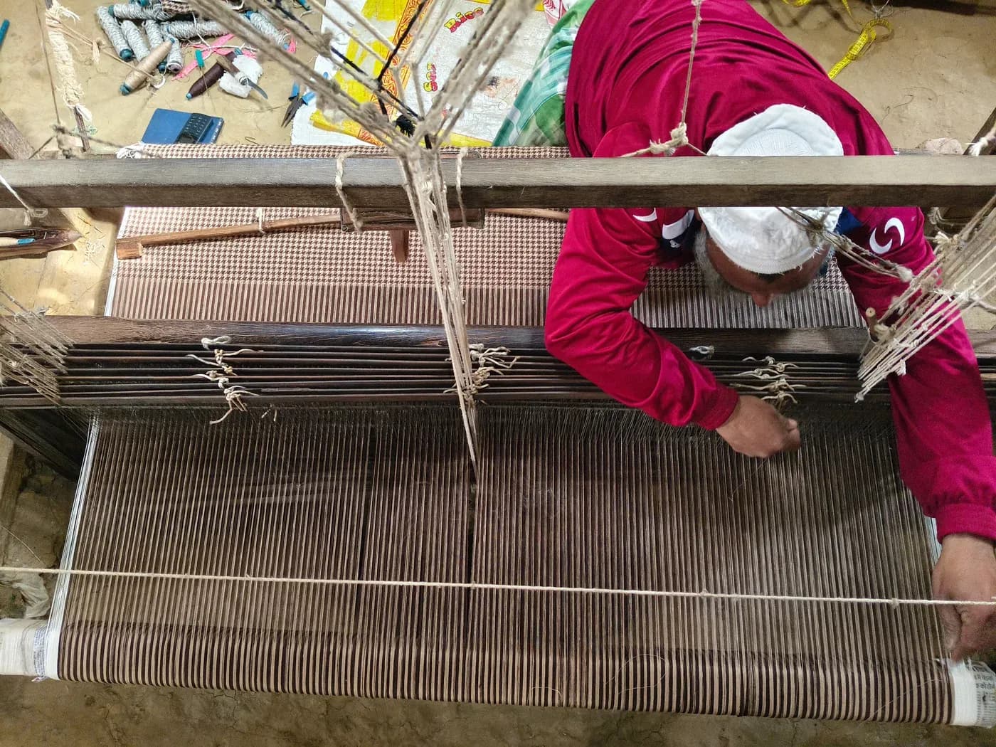 Overhead view of Mubarak weaving fine checkered fabric on a handloom